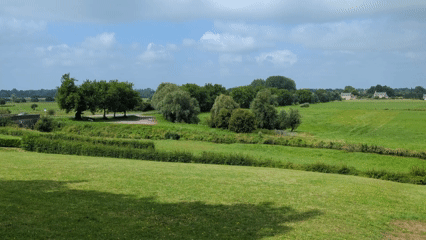 Panning shot of a flat green marsh ending with four bronze statue overlooking it