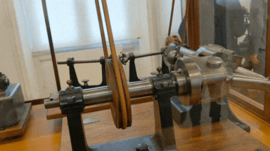 A rod with Y-shaped arms and universal joints slowly turns another Y-shaped rod at rightangles, before redirecting the movement through another smaller rightangle universal joint on the other side of a glass case.