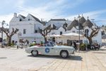 A 1950s open top grey Aston Martin sportscar stops in front of a whitewashed cafe in Bari,