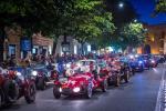 A procession of colourful 1000 Miglia vintage racing cars on the night streets of Bologna