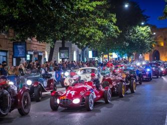 A procession of colourful 1000 Miglia vintage racing cars on the night streets of Bologna