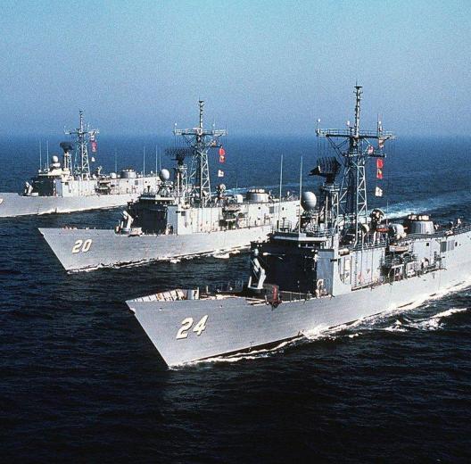 Three Cold War era US Navy frigates steaming through blue waters in line abreast