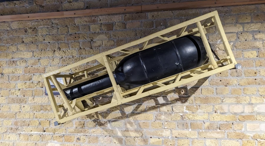 A fat black rocket in a sand coloured metal launch frame, displayed on a brick wall in the Dynamo Museum