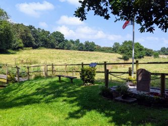 View from a shaded wood across sunny fields with a memorial stone in the foreground