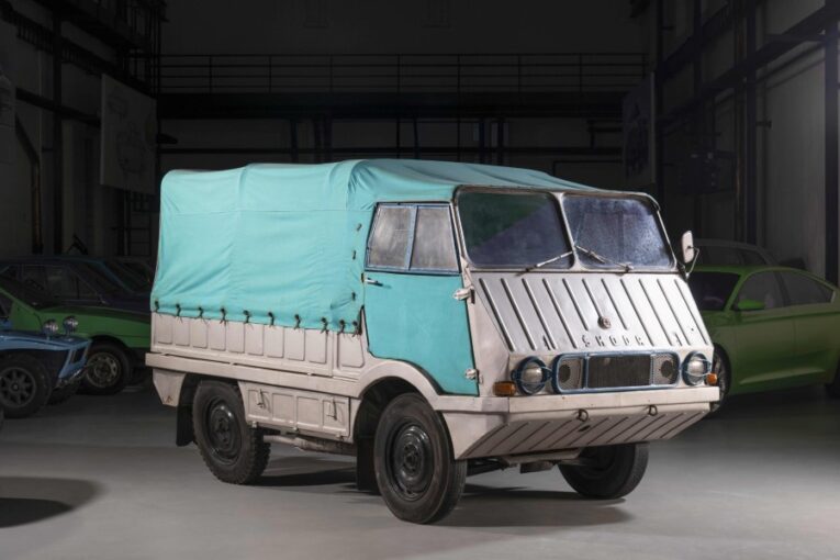 A light grey Škoda pickup truck with a blue canvas canopy over the cargo bed. It has a sloping glacis making it look like an amphibious truck.