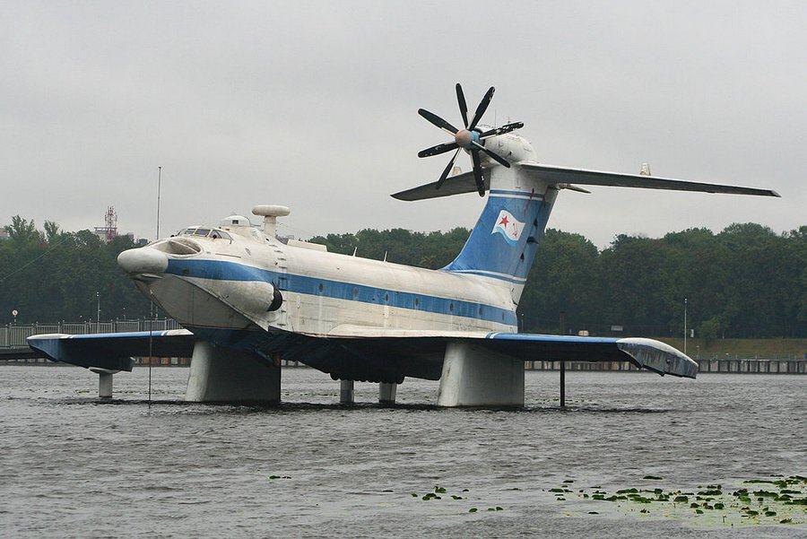 A large blue & white passenger carrying ekranoplan displayed on pylons over the water in a Moscow park