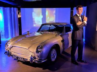 A not-very-lifelike dummy of James Bond in dinner jacket and with a gun, stands next to his silver grey Aston Martin DB5