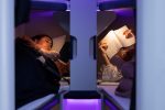 Two passengers lie close to each other in Air New Zealand Skynest bunks under purple lighting