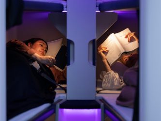 Two passengers lie close to each other in Air New Zealand Skynest bunks under purple lighting