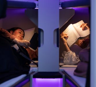 Two passengers lie close to each other in Air New Zealand Skynest bunks under purple lighting