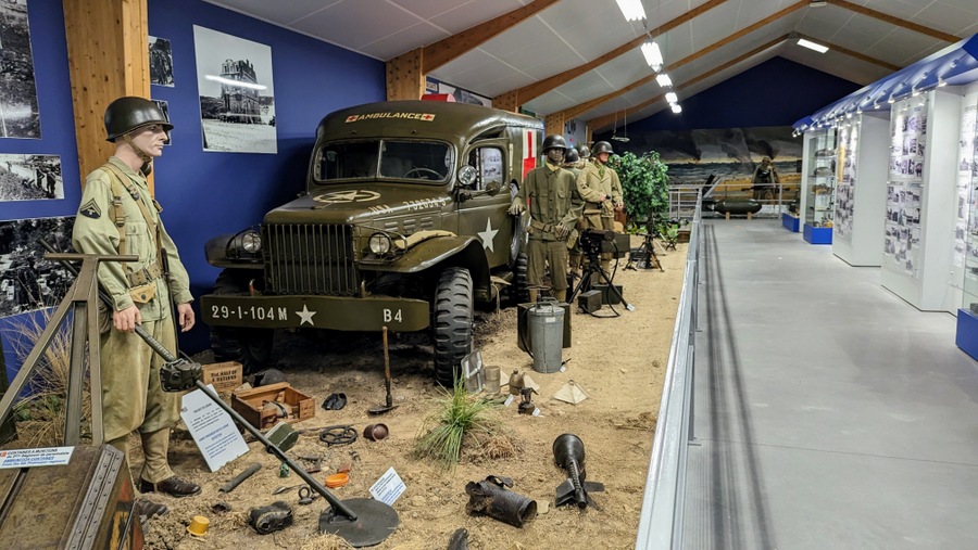 Diorama with a US Army Ambulance on the left and a wall of photos and documents on the opposite side of the aisle