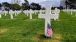 A white cross with a US flag planted in front of it, and many more white crosses stretching away into the distance behind it. The cross is for Joe J. Martinez from California, a private in the 112th combat engineering battalion
