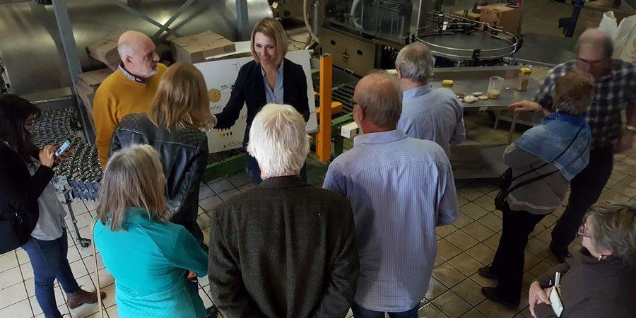 A factory tour group stand listening to a young woman explaining the workings of a micro-brewery