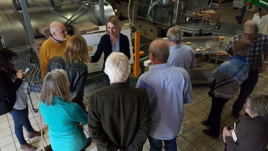 A factory tour group stand listening to a young woman explaining the workings of a micro-brewery