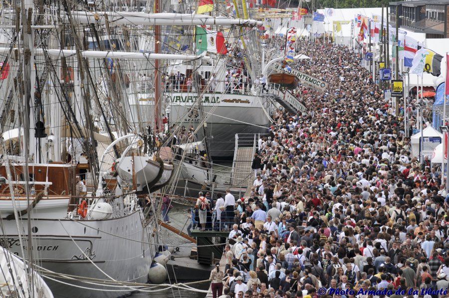 Large crowds promenade past the tall ships on the quayside in Rouen