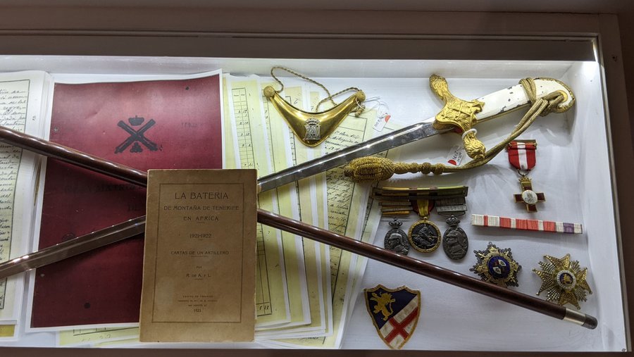 A sword, some medals and documents in a display case