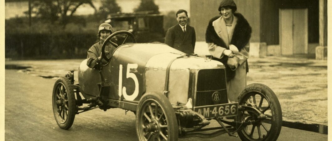 Black & white photo of three people posing in and behind the Aston Martin A1 sports car with a large white number 15 painted on it.