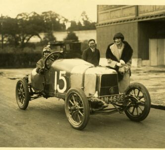 Black & white photo of three people posing in and behind the Aston Martin A1 sports car with a large white number 15 painted on it.