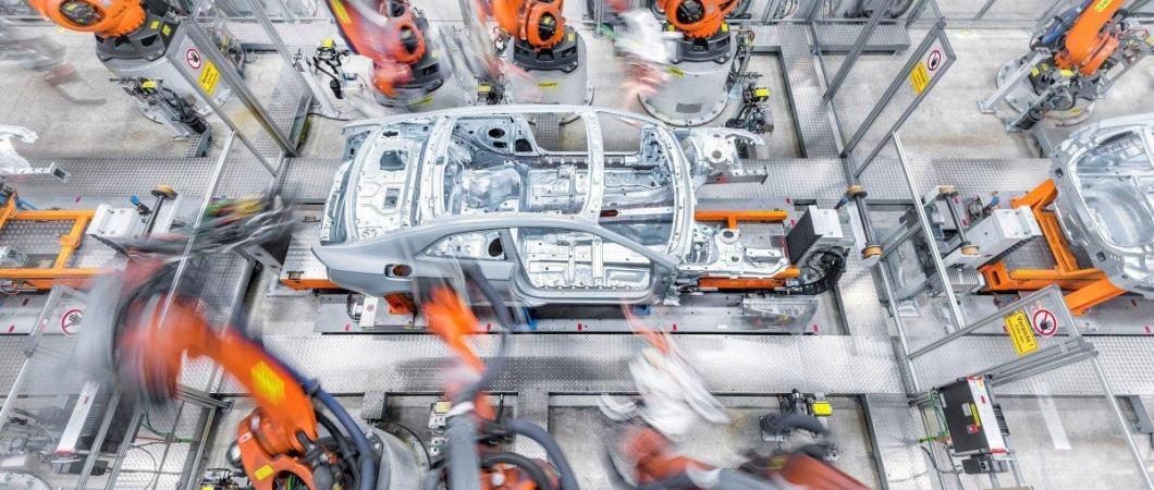 Fast moving orange robot arms work on a car chassis in the Audi factory