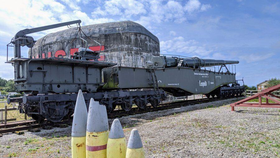 Some yellow artillery shells in the foreground with the railway gun behind