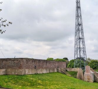 A large concrete bunker partially cover with a grassy bank, and a radio mast behind