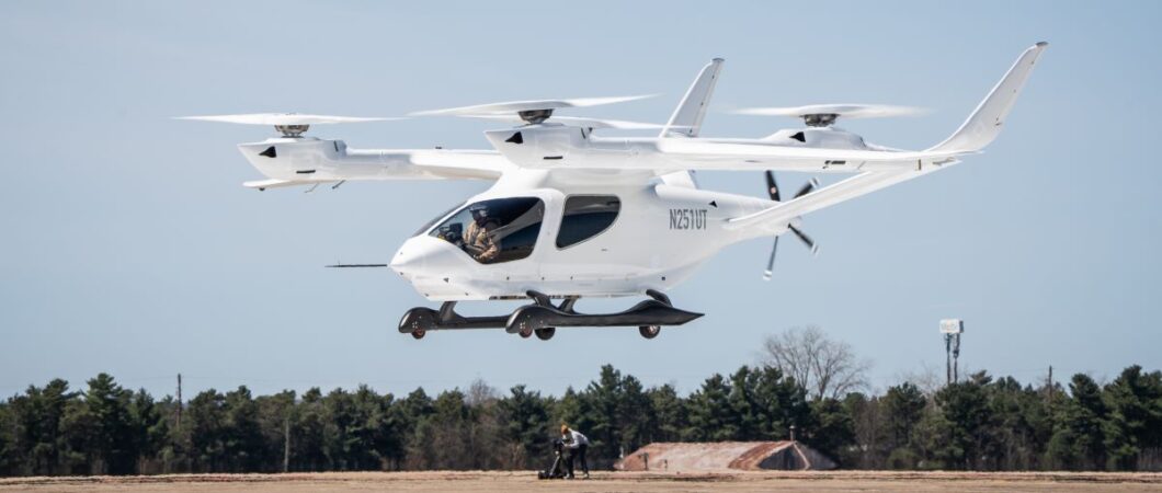 A white multi-rotor eVTOL hovers above the ground