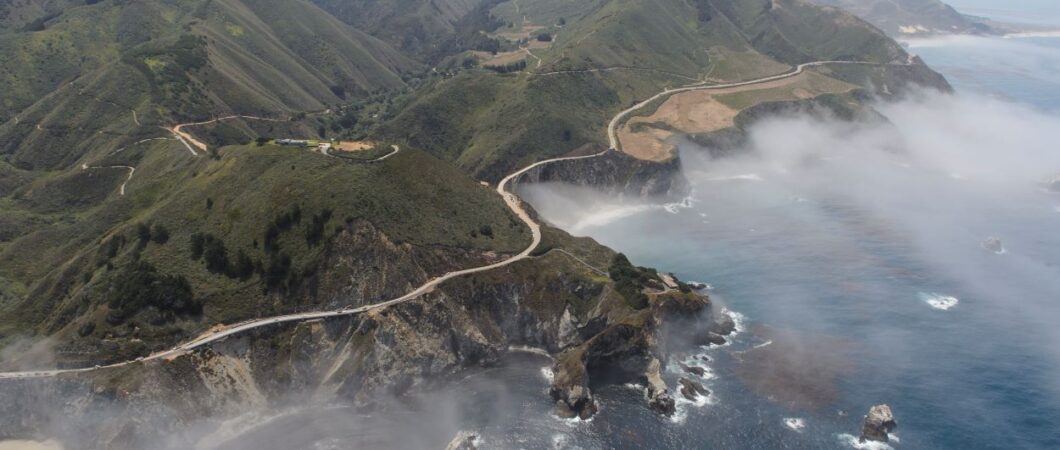 Aerial photo of Highway 1 coiling around the misty cliffs and headlands of Big Sur, and across Bixby Bridge.
