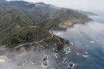 Aerial photo of Highway 1 coiling around the misty cliffs and headlands of Big Sur, and across Bixby Bridge.