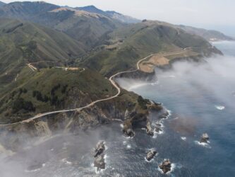Aerial photo of Highway 1 coiling around the misty cliffs and headlands of Big Sur, and across Bixby Bridge.