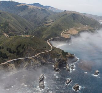 Aerial photo of Highway 1 coiling around the misty cliffs and headlands of Big Sur, and across Bixby Bridge.
