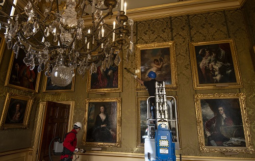 Cleaners vacuuming the library walls of Blenheim Palace, carefully working their way around large antique oil paintings