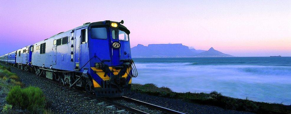 Blue painted diesel loco pulling the luxury coaches on a piece of track by the mauve coloured sea at sunset