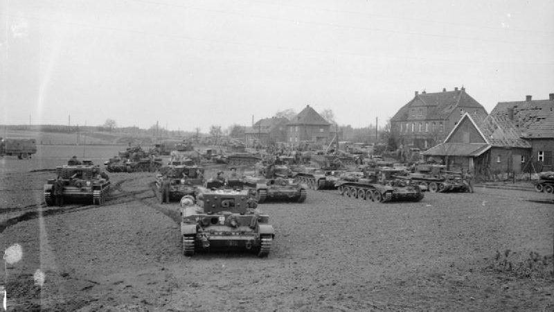 Black & white photo. A crowd of tanks on the outskirts of a village