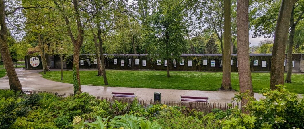 A long low, dark walled, concrete bunker with art posters on the walls at regular intervals, sits among the trees and grass of a municipal park