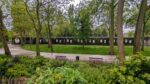 A long low, dark walled, concrete bunker with art posters on the walls at regular intervals, sits among the trees and grass of a municipal park