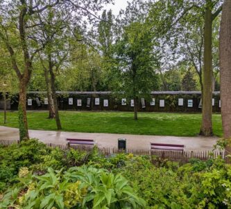 A long low, dark walled, concrete bunker with art posters on the walls at regular intervals, sits among the trees and grass of a municipal park