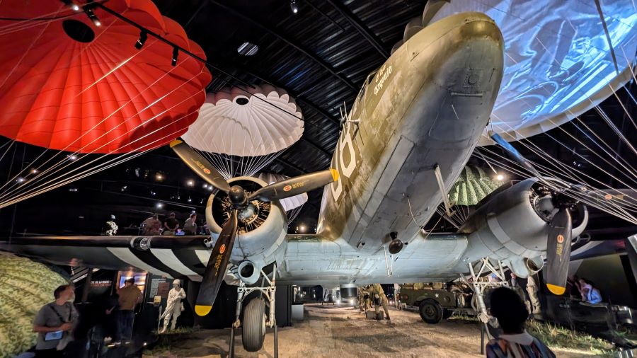 The nose of a C-47 transport aircraft looms up in the dark surrounded by colourful parachute canopies