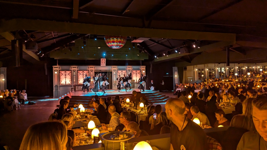 Waiters on a stage dance surrounded by the restaurant diners