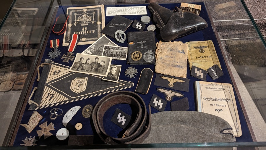 A glass encased cabinet with personal items and equipment such as photographs, uniform badges, and flags