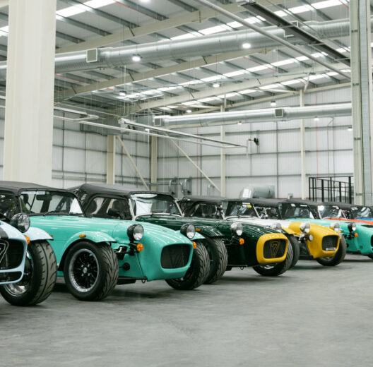 A row of multi-coloured sports cars in a large new hanger-like building