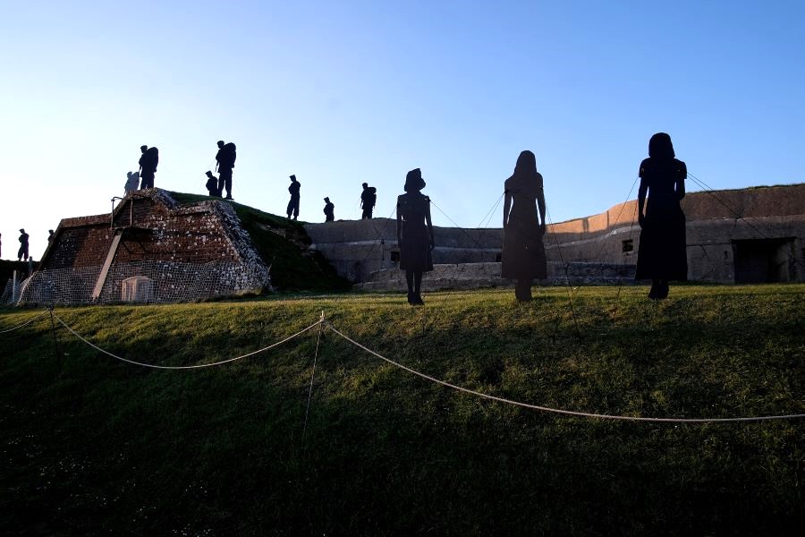 Falklands Tribute silhouettes on top of the Nothe Fort ramparts on a sunny day and in the gloomier foreground three silhouettes of women civilians