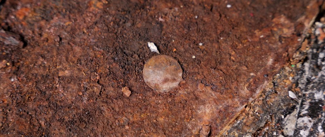 A small corroded brown coin on a rusty surface