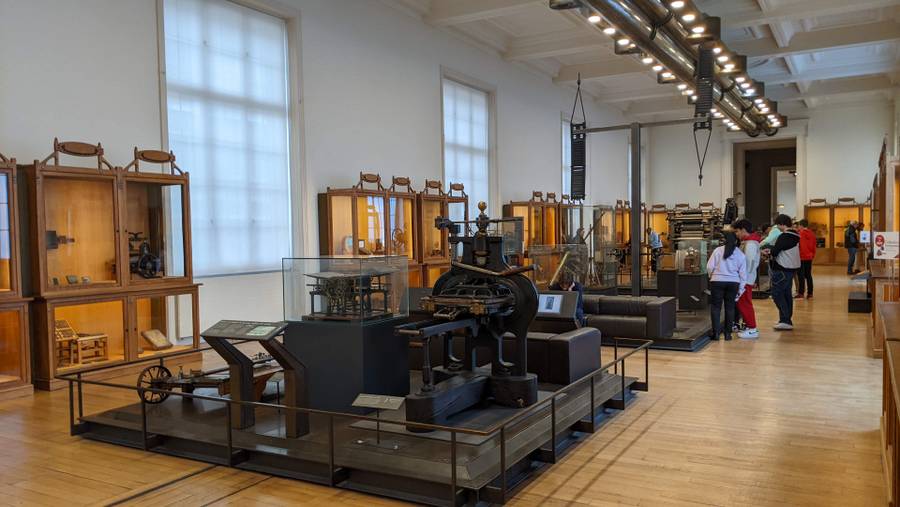 Large hall with printing presses and other devices in the centre and display cases on the walls