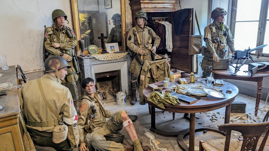 Soldiers (mannequins) relax leaning against the wall or sitting on the floor. There is a machine gun mounted on a table by the window.