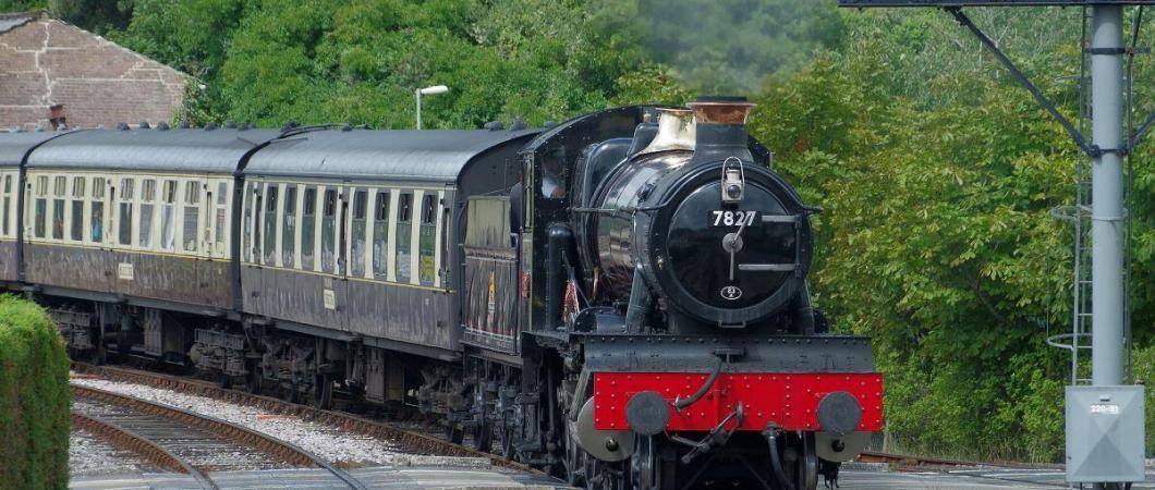 A black steam locomotive with vintage coaches behind, approaches the camera