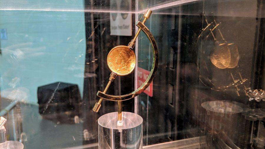 a dented gold coin in a museum display case
