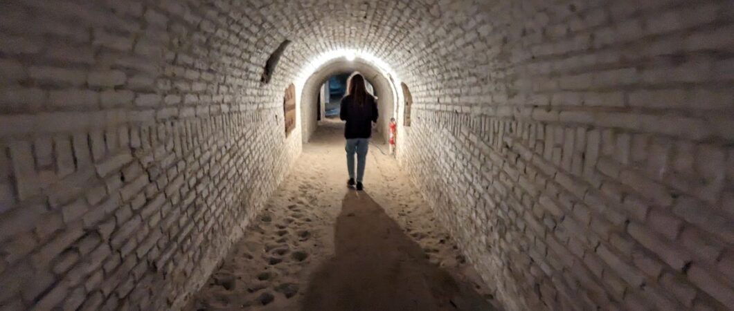 A woman walks down a long brick underground corridor