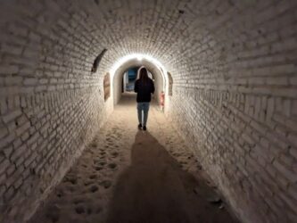 A woman walks down a long brick underground corridor