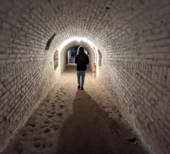 A woman walks down a long brick underground corridor