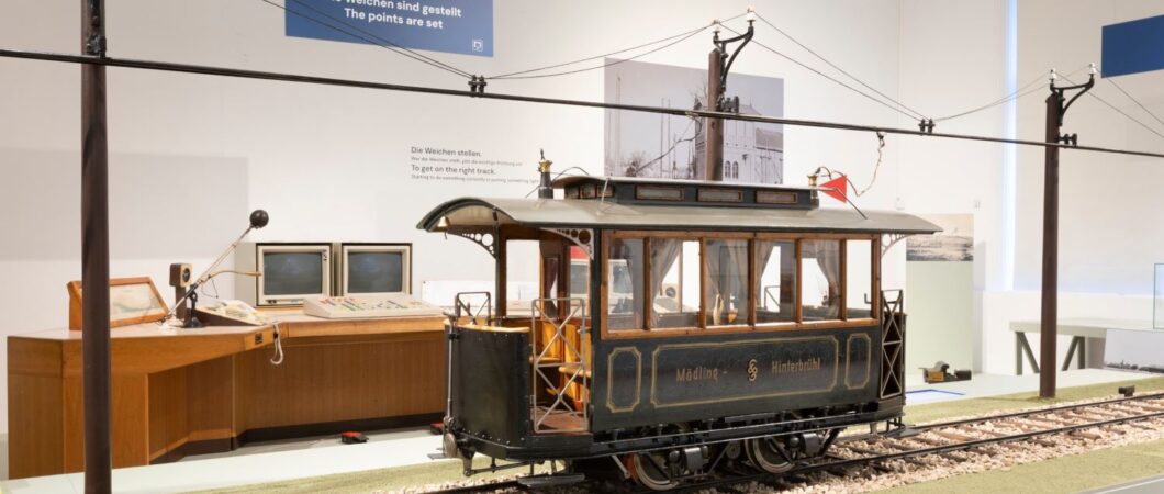 A large scale model of an early Austrian tram displayed on a track with the electric catenary above